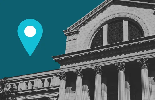 Smithsonian National Museum of Natural History building seen from the south, or National Mall, side. The entrance has six tall, stone columns with a pediment above them containing a semi-circular window. A blue and white map pin graphic is on the left side of the image, in the sky next to the building.
