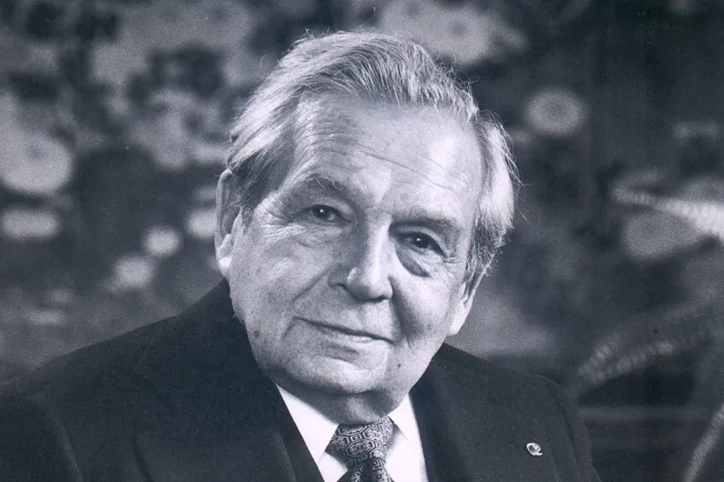 Portrait of a light-skinned man in a suit holding a pair of glasses