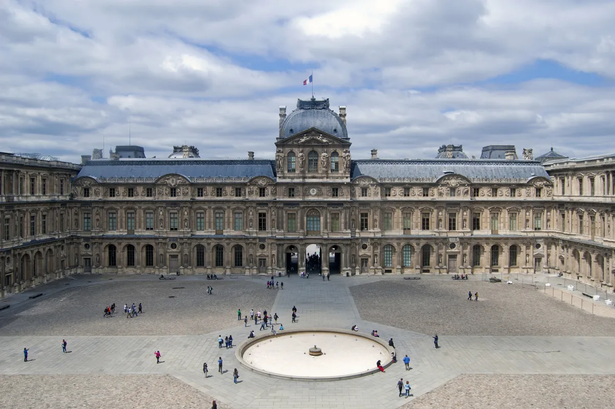 People milling on a stone plaza in front of the Louvre