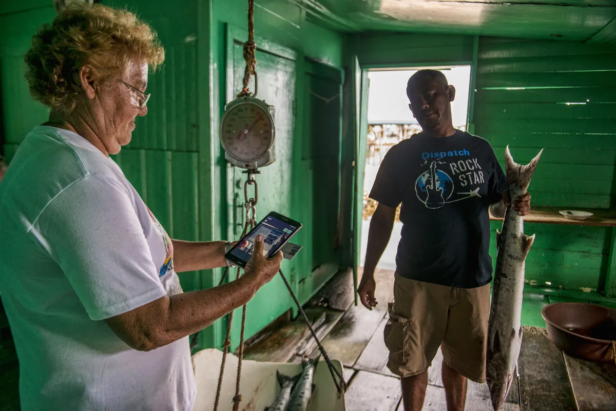 A woman looks at a fish app on her cell phone while a man looks on. 